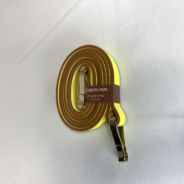 A alça de ombro amarela com acessórios dourados é enrolada e a etiqueta castanha "ROBERTA PIERI shoulder strap 110 cm" é adornada na superfície branca.