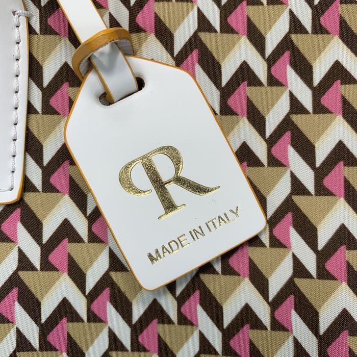 Um close-up de uma etiqueta de bagagem branca Roberta Pieri com a inscrição "R" em ouro e as palavras "MADE IN ITALY" anexadas a uma mini bolsa duffel com padrões geométricos castanhos, beges e rosas.