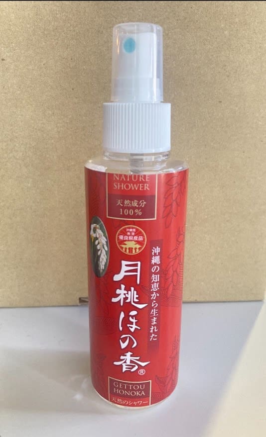 Um frasco de spray vermelho com as palavras "Nature Shower" escritas em um fundo bege. Bico e tampa de pulverização brancos.